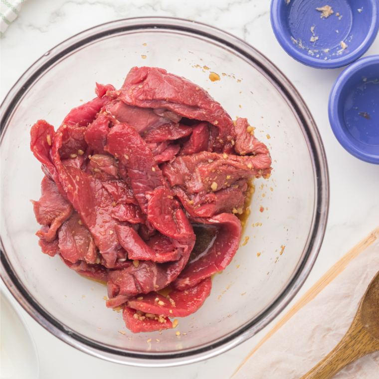 Steak strips marinating in soy, oyster, and sesame sauce in a bowl