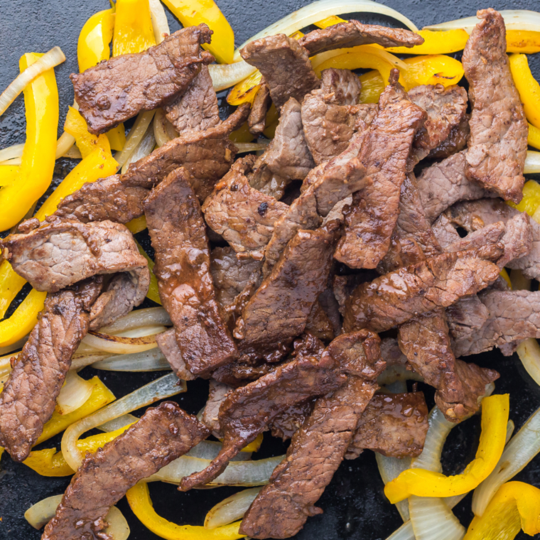 Udon noodles tossed in sauce on a Blackstone griddle with a spatula