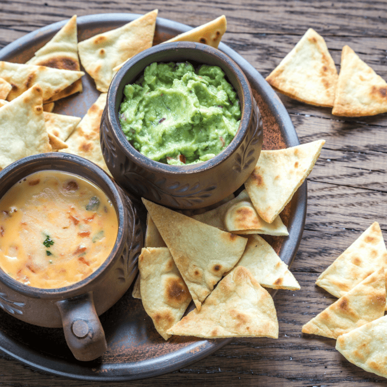 Delicious Carlos O'Kelly's Queso Recipe served in a bowl, with chunks of tomato and onion, and surrounded by crispy tortilla chips.