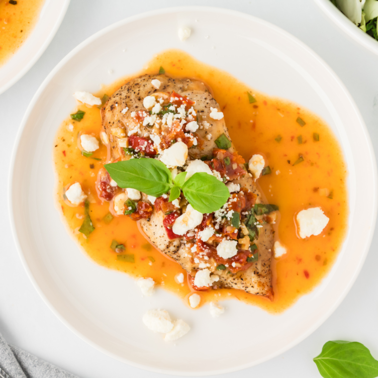 Plated chicken breast topped with lemon butter sauce, crumbled goat cheese, and fresh basil garnish.