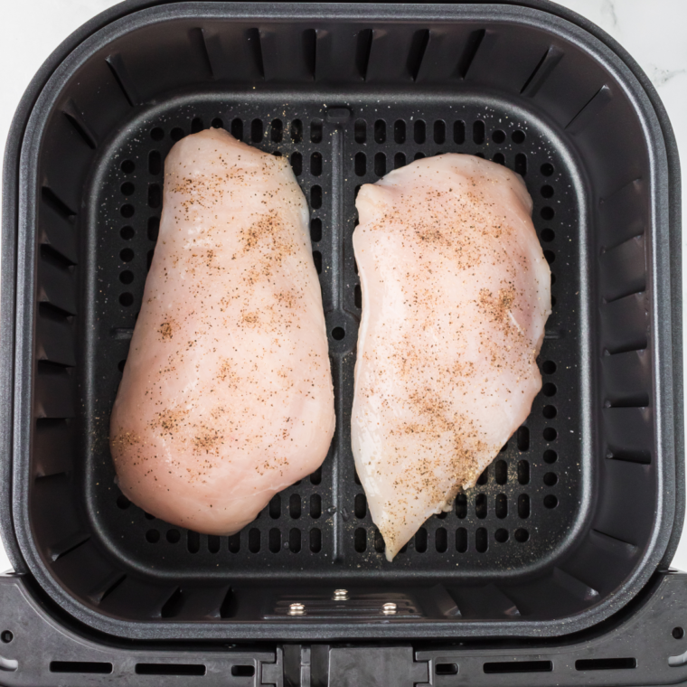 Lightly seasoned chicken breasts with salt and pepper on a cutting board.