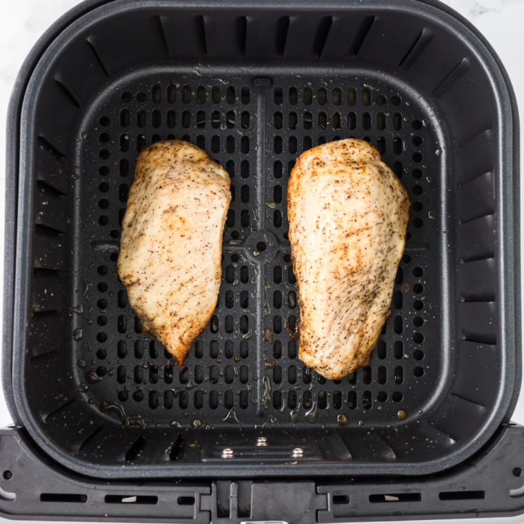 Chicken breasts brushed with olive oil arranged in an air fryer basket set to 380 degrees F for cooking.