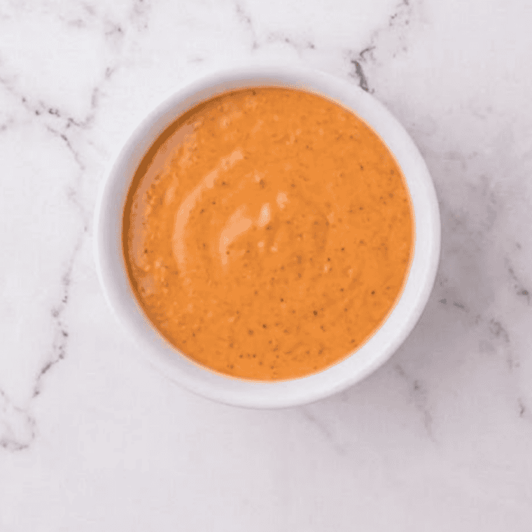Copycat McDonald's buffalo sauce in a bowl with a chicken nugget being dipped