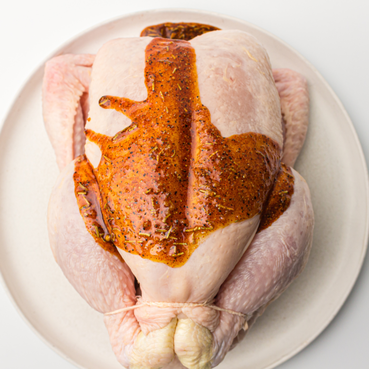 Chicken rubbed with olive oil and seasoned with a flavorful spice mix, ready to cook for a delicious rotisserie-style meal."