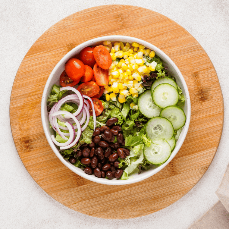 Assembling the salad with greens, veggies, and BBQ chicken