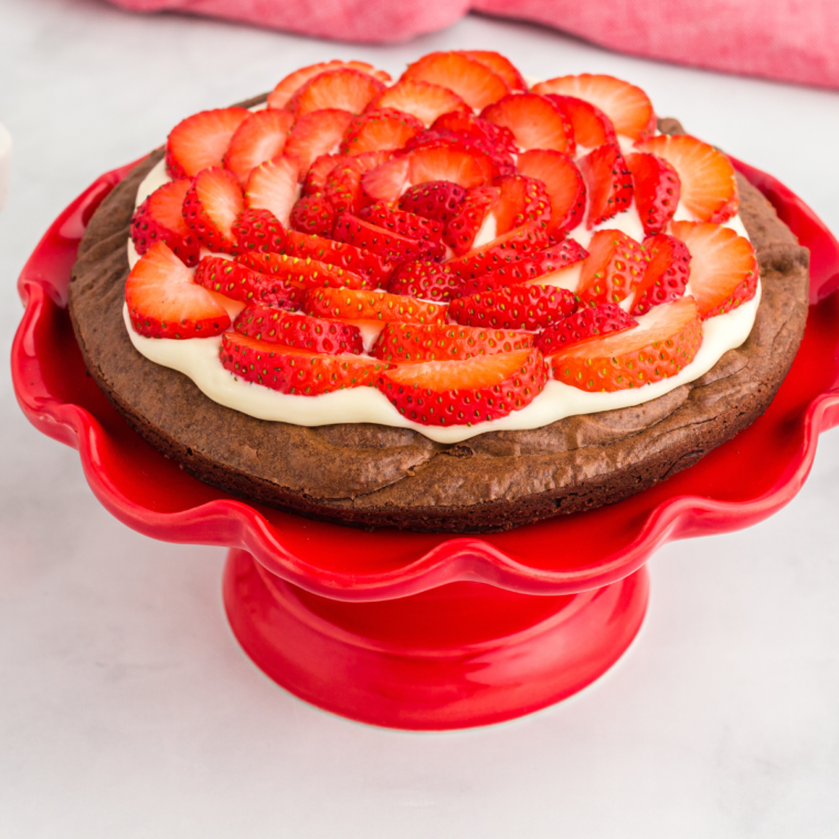 Air fryer brownie pizza with pink frosting and sliced strawberries on a red plate