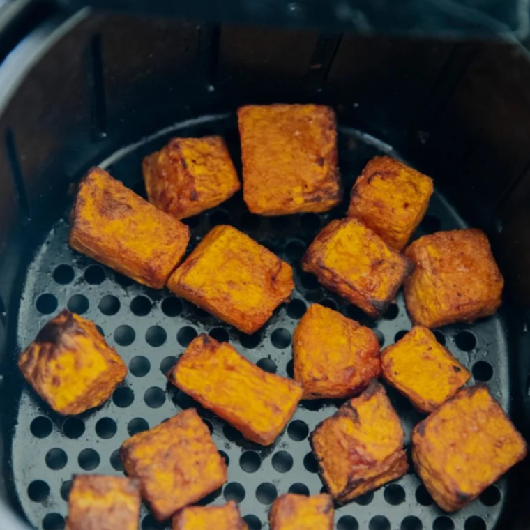Air fryer basket being shaken halfway through cooking to brown the butternut squash evenly