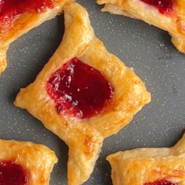 Golden, flaky Air Fryer Raspberry Danish with raspberry filling and a sweet glaze drizzle, served on a white plate.