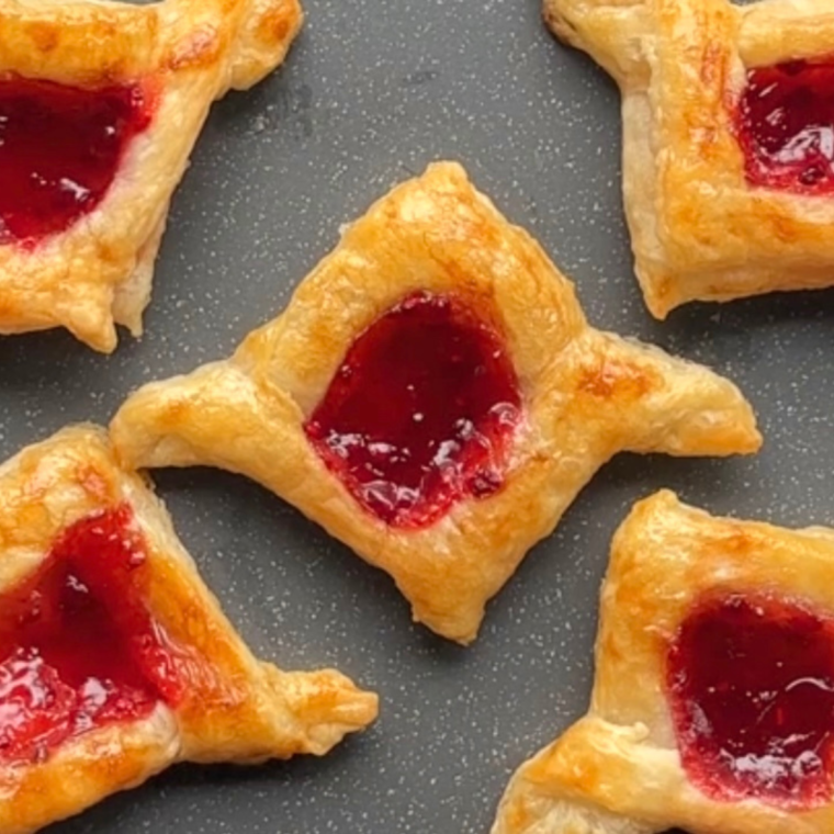 Flaky, golden Air Fryer Raspberry Danish with raspberry filling and drizzled glaze, served on a plate.