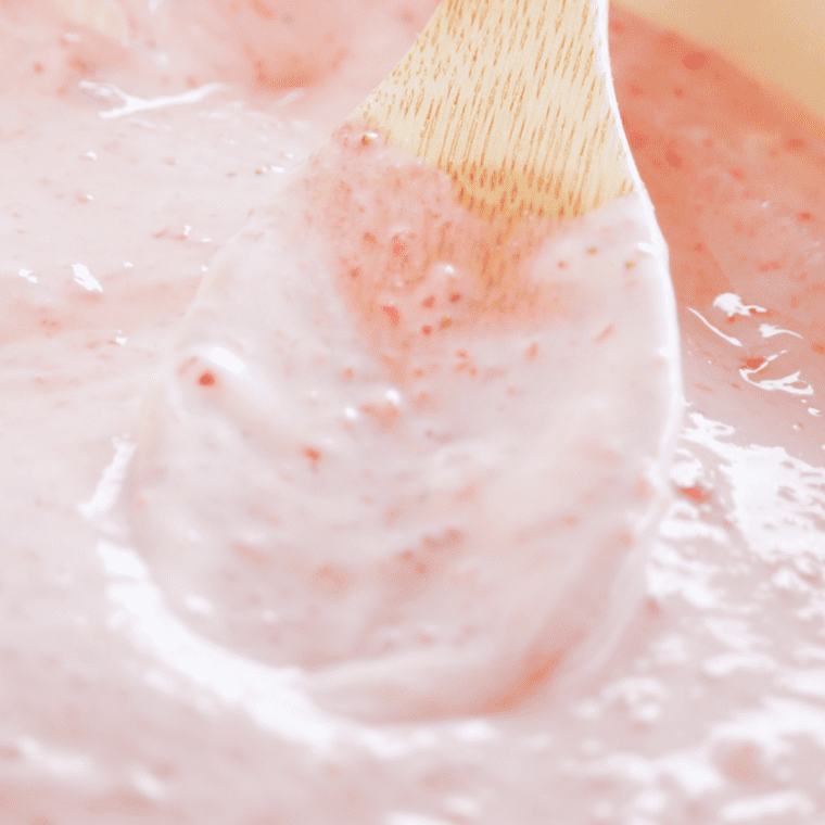 Pouring cream cheese filling over chilled graham cracker crust and swirling strawberry preserves to create a marbled cheesecake effect.