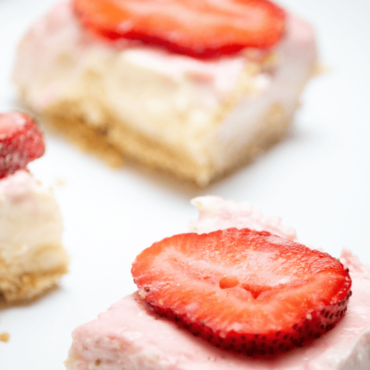 Air Fryer Strawberry Cheesecake Bars with marbled strawberry swirls on a graham cracker crust, garnished with fresh strawberry slices.