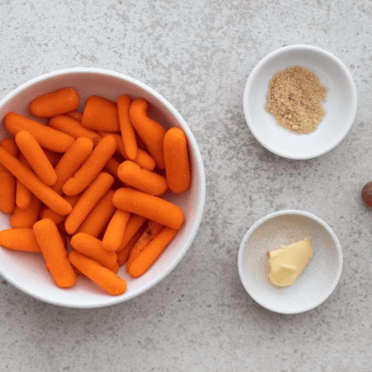 Ingredients for Cracker Barrel Carrots, including fresh carrots, brown sugar, butter, and seasonings, arranged on a wooden surface ready for cooking.