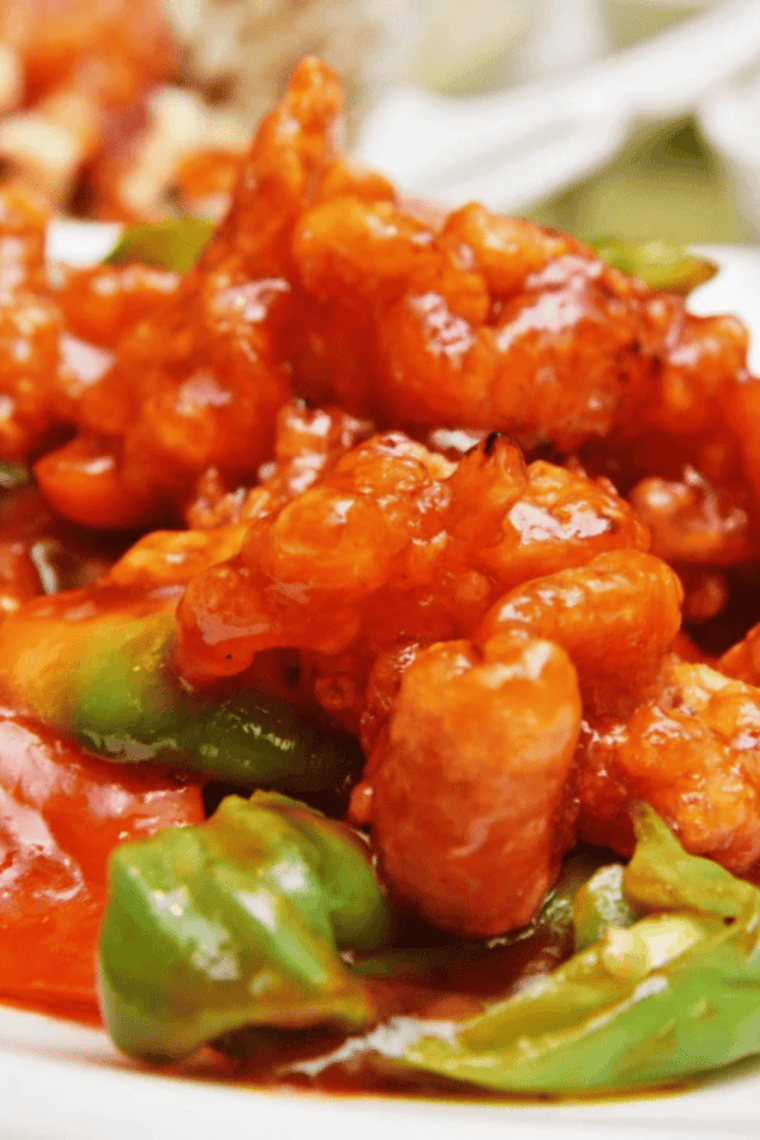 Crispy air fryer cauliflower coated in sweet and sour sauce, served in a white bowl with a sprinkle of green onions.