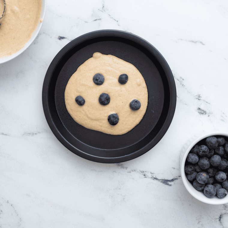 Blueberry pancake batter poured into pan and topped with blueberries