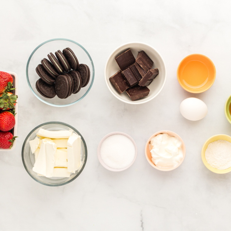 Ingredients for chocolate strawberry mini cheesecakes: cream cheese, sugar, egg, Oreos, chocolate, and strawberries