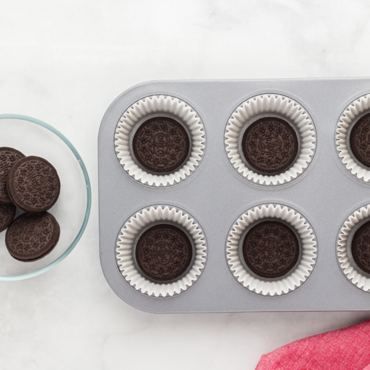 Oreo cookies placed in the bottoms of cupcake liners in a muffin tin