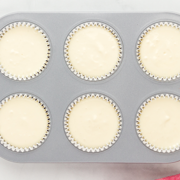 Spooning cheesecake batter over the Oreo crust in each cupcake liner