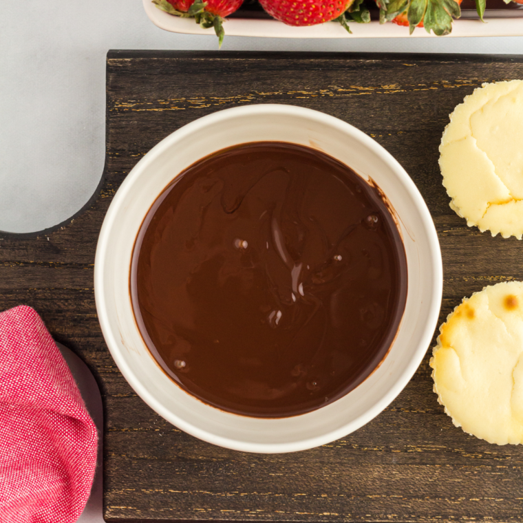 Chilled mini cheesecakes ready for their melted chocolate and strawberry topping