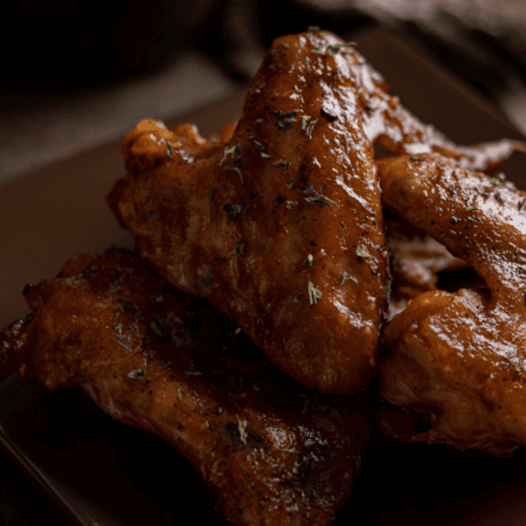Crispy Air Fryer Coca Cola Wings coated in a caramelized glaze, served on a plate and garnished with fresh herbs.