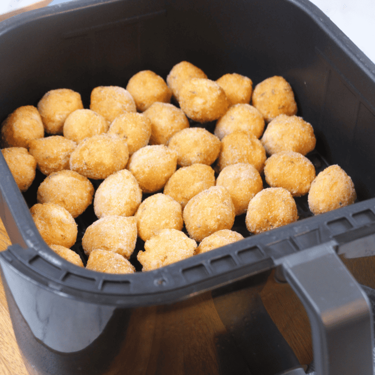 Frozen hush puppies arranged in a single layer in an air fryer basket before cooking