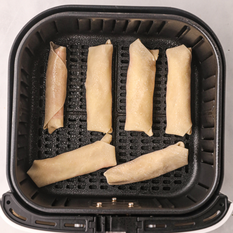 Uncooked pizza egg rolls in air fryer basket sprayed with olive oil before cooking