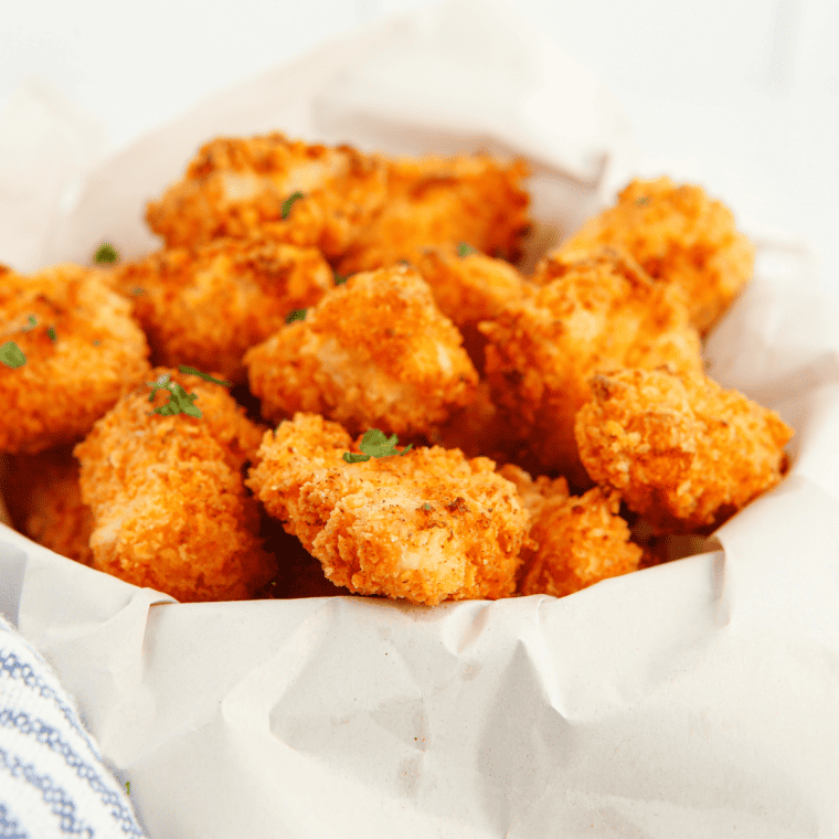 Golden crispy air fryer popcorn chicken piled on a plate with dipping sauce on the side