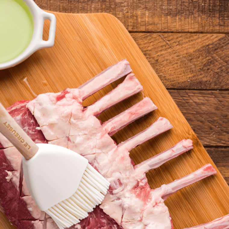 Rack of lamb being brushed with olive oil and seasoned generously with mixed spices and herbs.