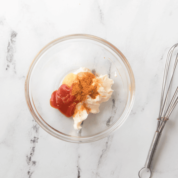 Whisking mayonnaise and ketchup together in a glass mixing bowl