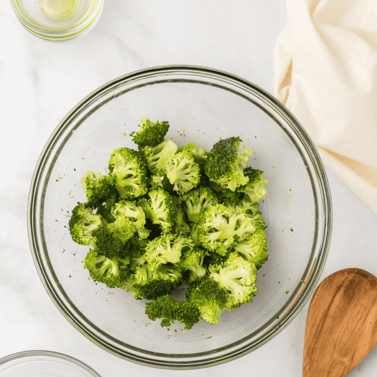 tossing broccoli florets with oil salt and pepper in mixing bowl before cooking