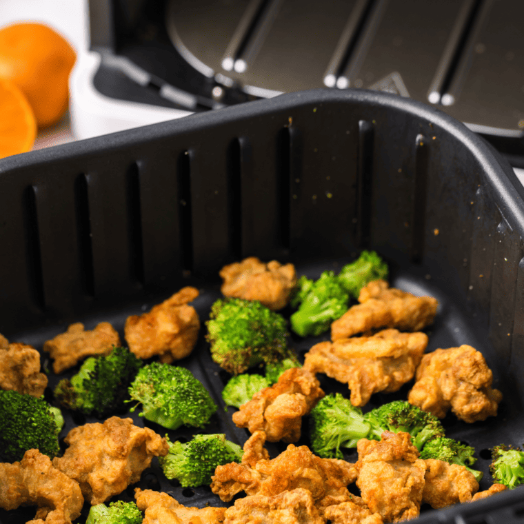 shaking air fryer basket while chicken and broccoli cook until crispy and tender