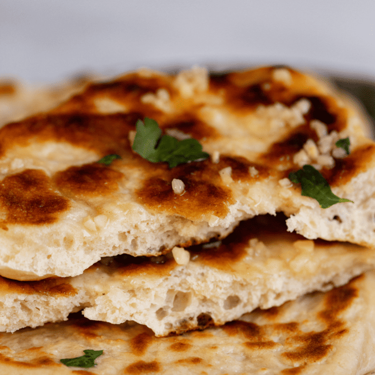 Freshly cooked Blackstone Naan on the griddle, golden brown with soft, pillowy texture, ready to serve
