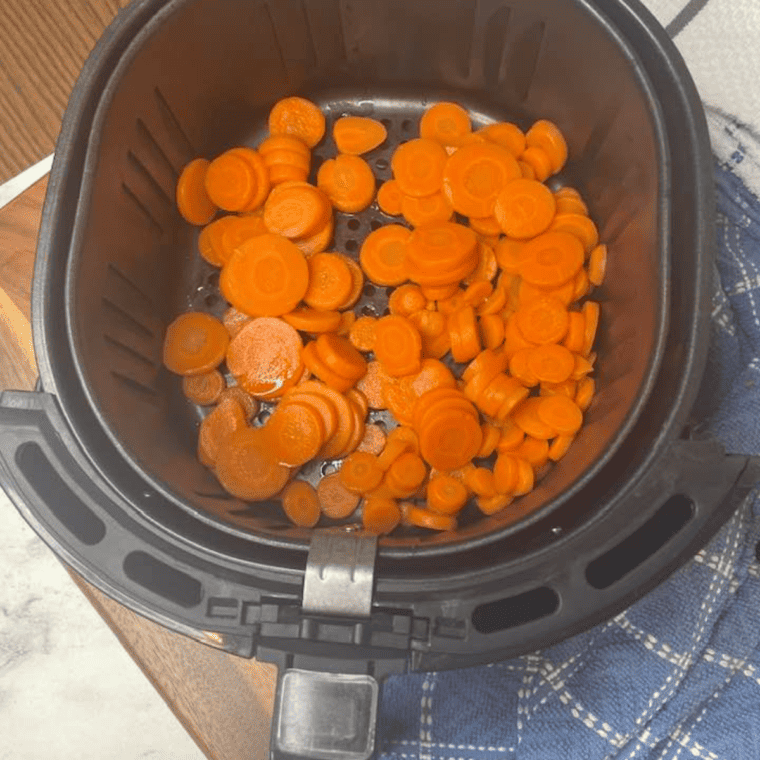 Seasoned canned carrots spread in an air fryer basket, cooking evenly while being shaken during roasting.
