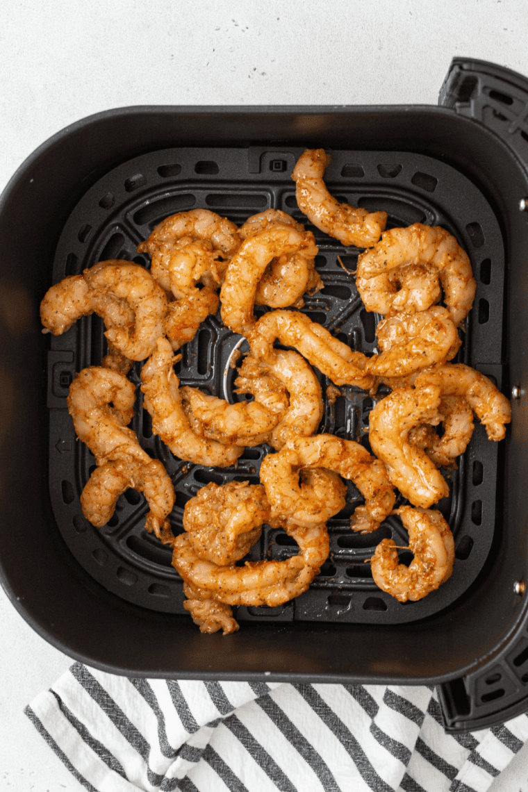 Shrimp cooking in a single layer in the air fryer basket.