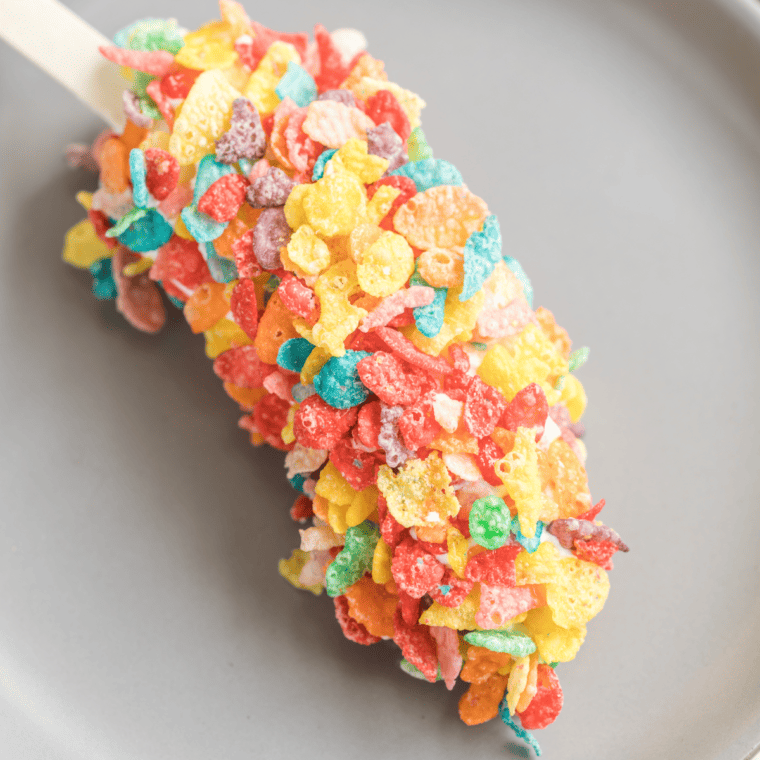 Easy Fruity Pebbles Banana Pops arranged on a tray, coated in yogurt and colorful cereal, ready to enjoy.