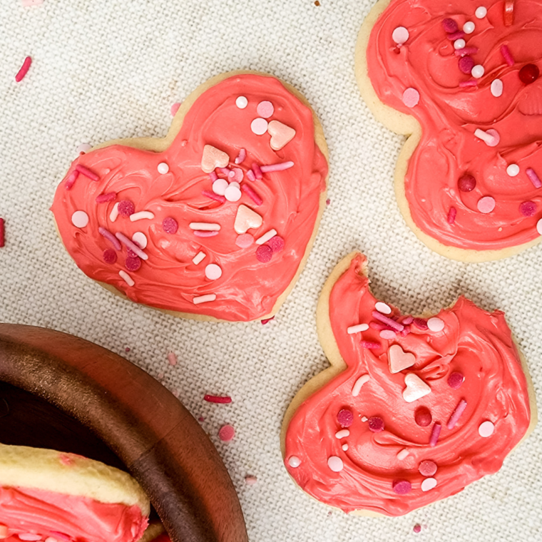 Heart-shaped Valentine’s Day Lofthouse Cookies with pink frosting and rainbow sprinkles on a plate