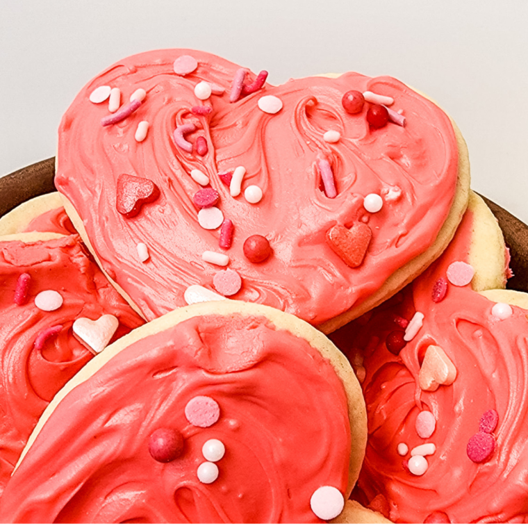 Heart-shaped Valentine’s Day Lofthouse Cookies topped with pink frosting and rainbow sprinkles on a plate