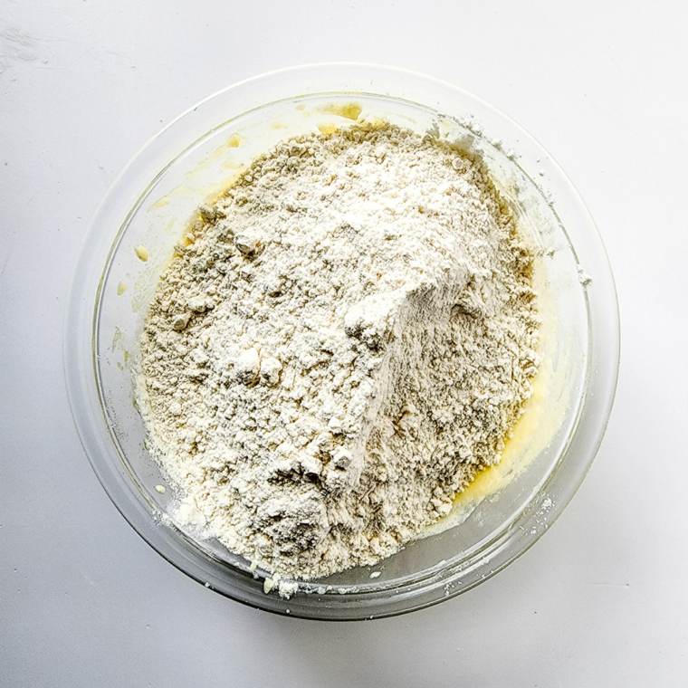 Dry ingredients being gradually mixed into wet cookie dough in a large bowl