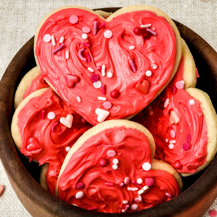 Heart-shaped Valentine’s Day Lofthouse Cookies topped with pink frosting and colorful sprinkles on a plate