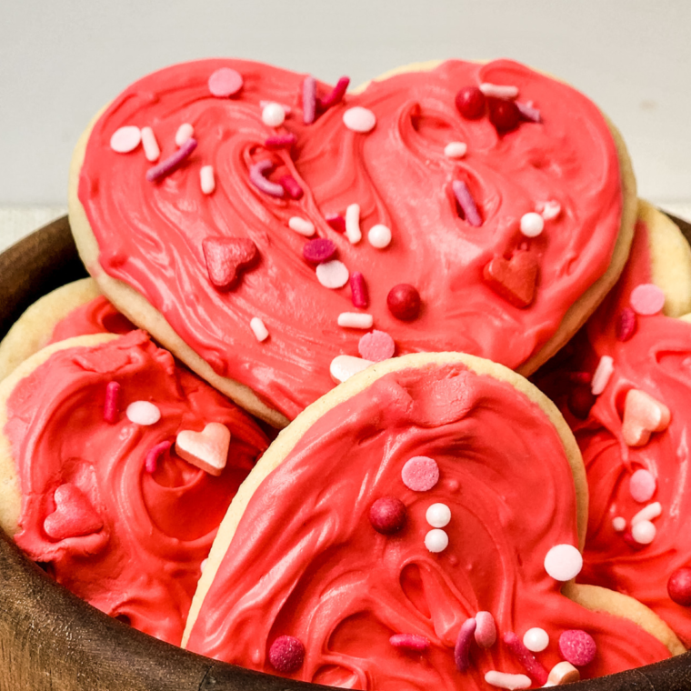 Heart-shaped Valentine’s Day Lofthouse Cookies with pink frosting and colorful sprinkles on a plate