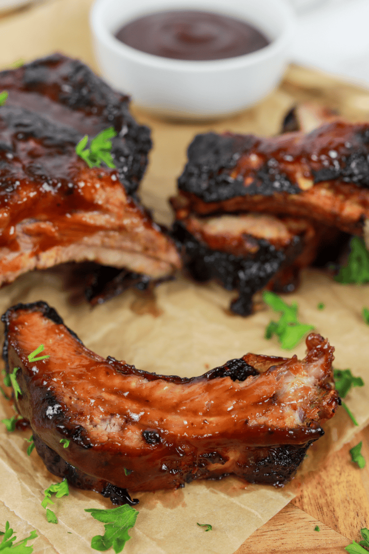 Glass jar of golden whiskey peach BBQ sauce with fresh peaches and a brush on a wooden board.