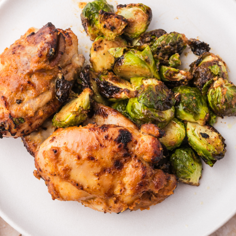 Roasted brussels sprouts and chicken thighs on a plate with Carolina Gold BBQ sauce drizzled over