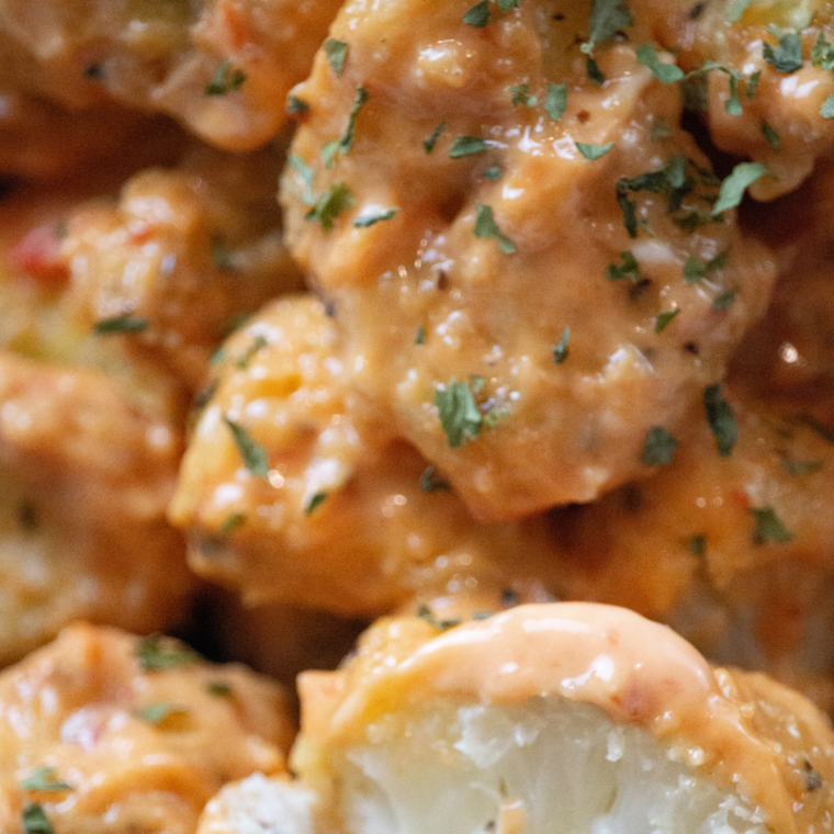 Golden brown and crispy Air Fryer Bang Bang Cauliflower coated in a flavorful sweet and spicy sauce, served with garnishes.