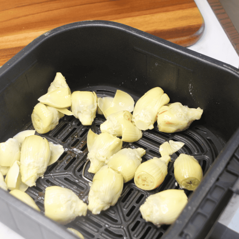 Quartered artichoke hearts tossed with olive oil and seasoning in a bowl