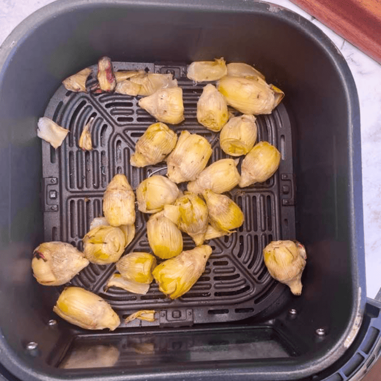 Canned artichokes in air fryer basket arranged in a single layer before cooking.