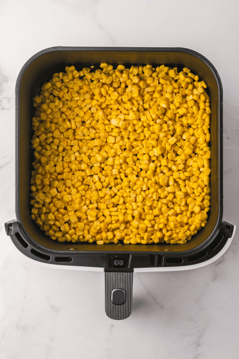 Spreading canned corn in a single layer in the air fryer basket, adding butter, garlic powder, salt, and pepper before air frying for 3-5 minutes.