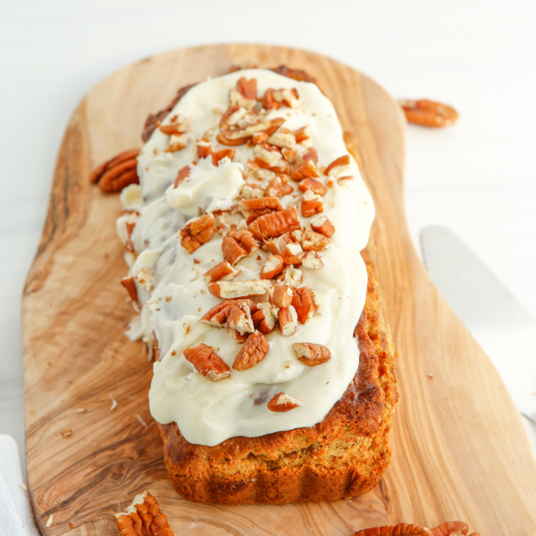 Air Fryer Carrot Cake Loaf topped with cream cheese frosting and sliced on a wooden board