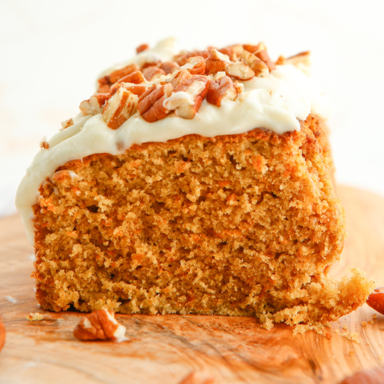 Sliced air fryer carrot cake loaf on a wooden board, topped with cream cheese frosting and sprinkled with chopped walnuts.
