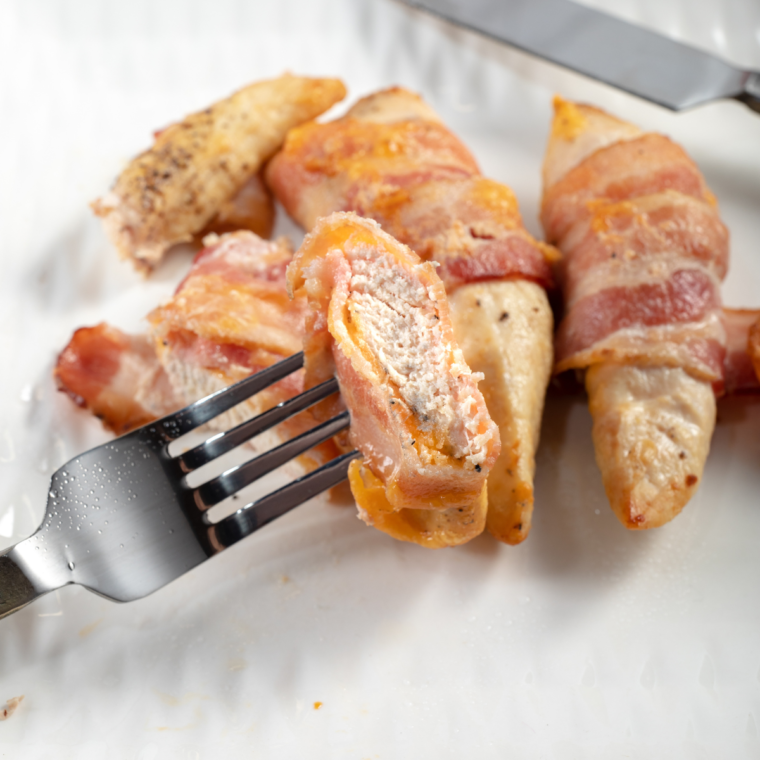 Close-up of air fryer bacon wrapped chicken with golden brown bacon and melted cheese oozing from the center