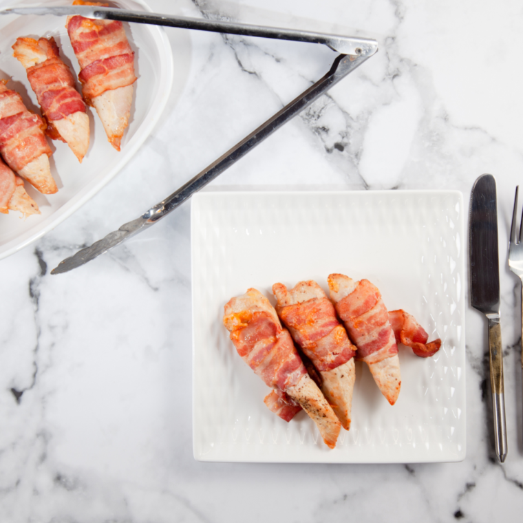 Chicken thighs wrapped in bacon cooking in an air fryer basket until crisp and browned