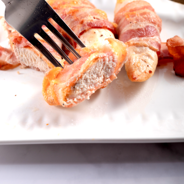 Air fryer bacon wrapped chicken stuffed with cheese served with browned crispy bacon on a cutting board